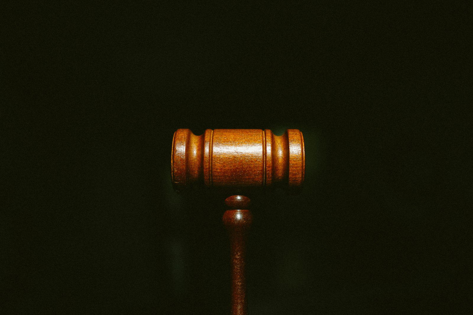 Wooden judges gavel resting on closed legal book on dark surface