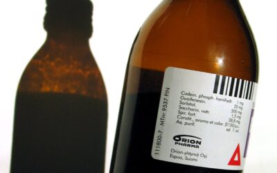 A bottle of cough syrup medicine with a dosage measuring cup