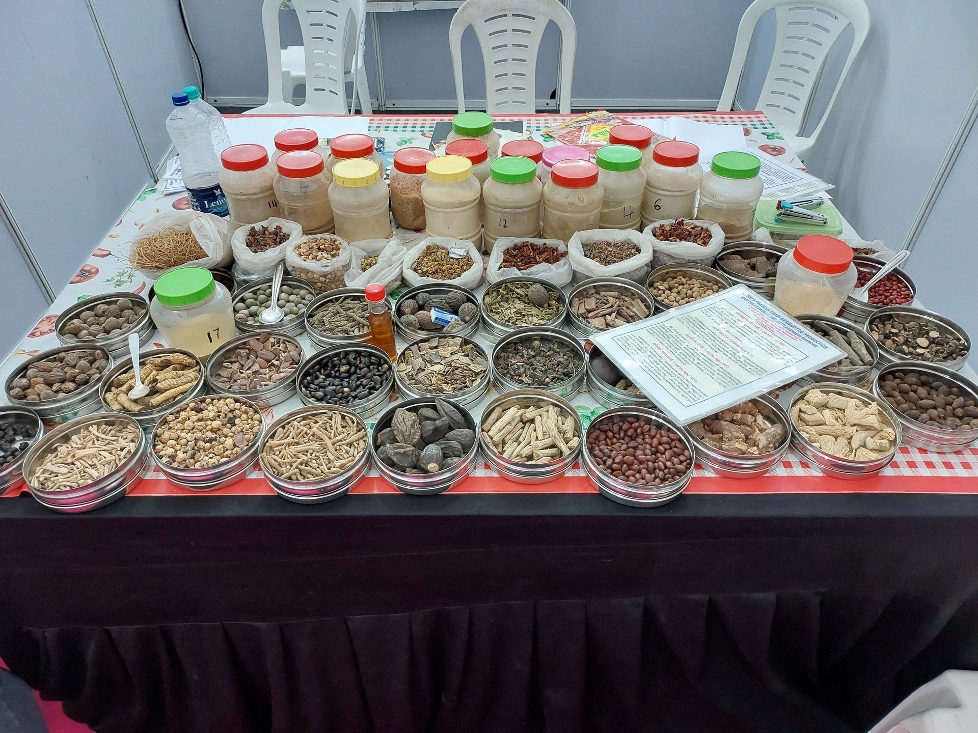 Bowls and jars of dried Ayurvedic medicinal herbs and roots displayed on a table at an exhibition