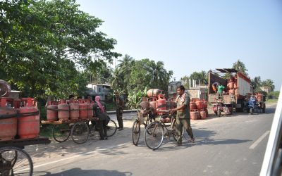 Delivery workers loading domestic LPG cylinders onto cycle carts beside a truck on a roadside