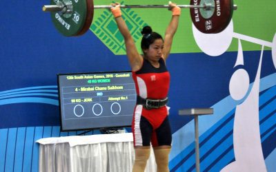 Weightlifter Saikhom Mirabai Chanu holding a loaded barbell overhead during a competition lift