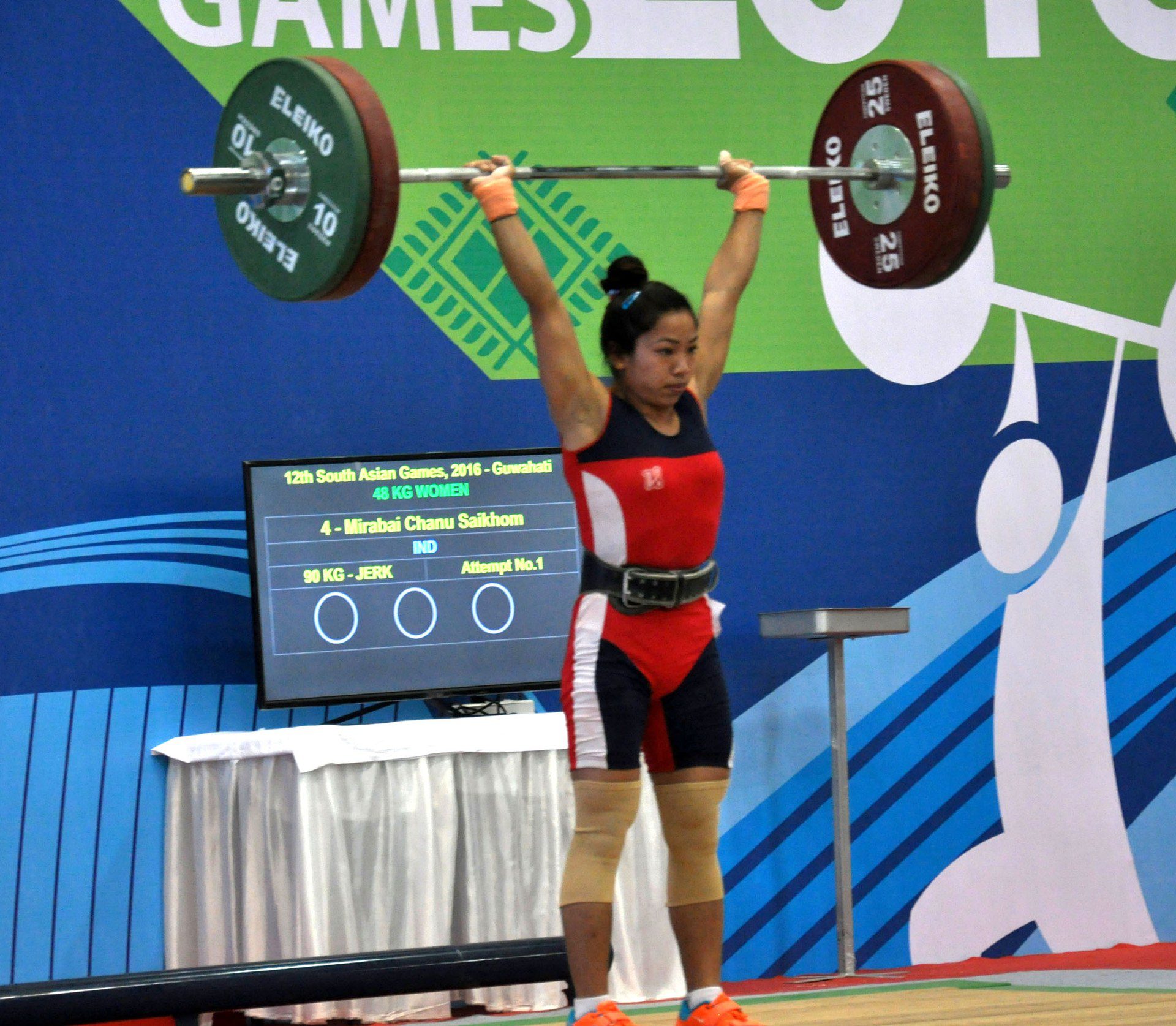 Weightlifter Saikhom Mirabai Chanu holding a loaded barbell overhead during a competition lift