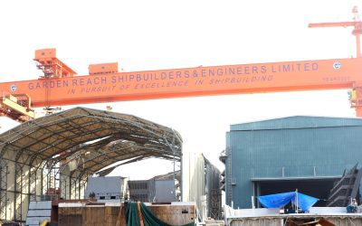 Orange gantry crane bearing the Garden Reach Shipbuilders and Engineers name over shipbuilding sheds in Kolkata