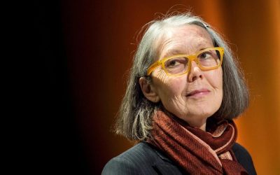 Canadian poet Anne Carson in yellow glasses and a red scarf on a stage in Stockholm
