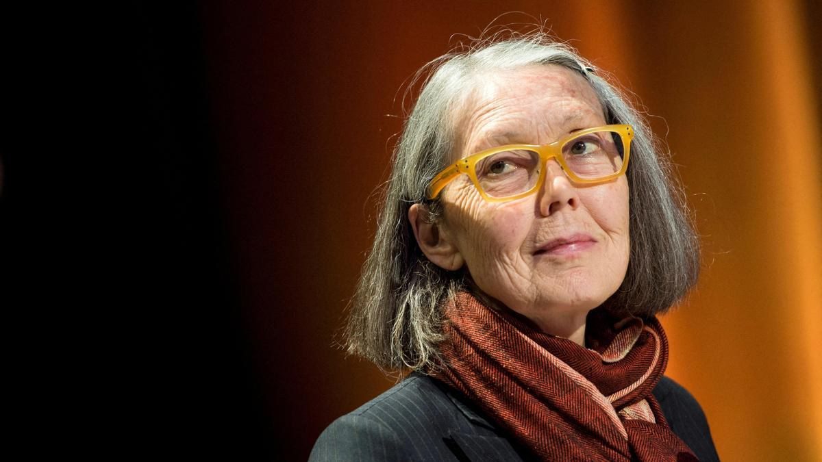 Canadian poet Anne Carson in yellow glasses and a red scarf on a stage in Stockholm